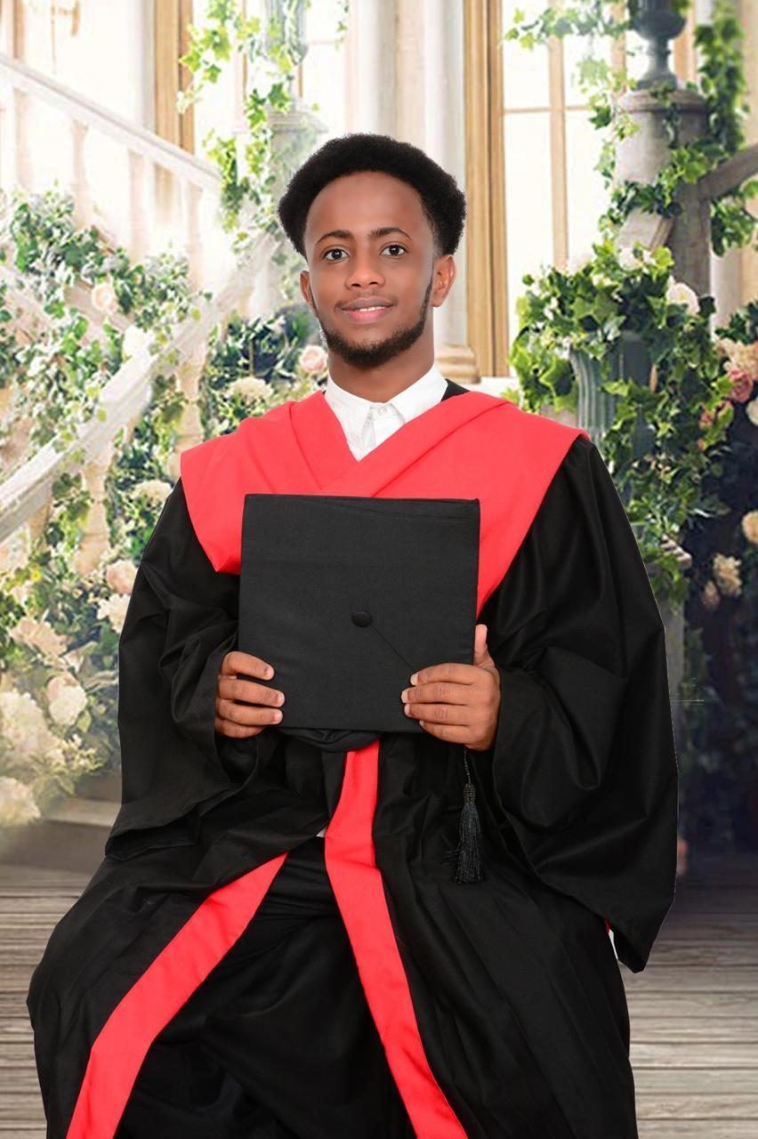 A Nuria College graduate in gown holding a cap